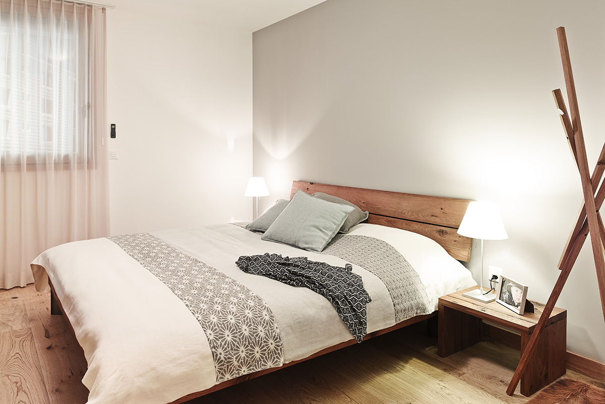 Cozy bedroom in a vacation apartment in Switzerland with minimalist wooden furniture, soft lighting, and modern decor.