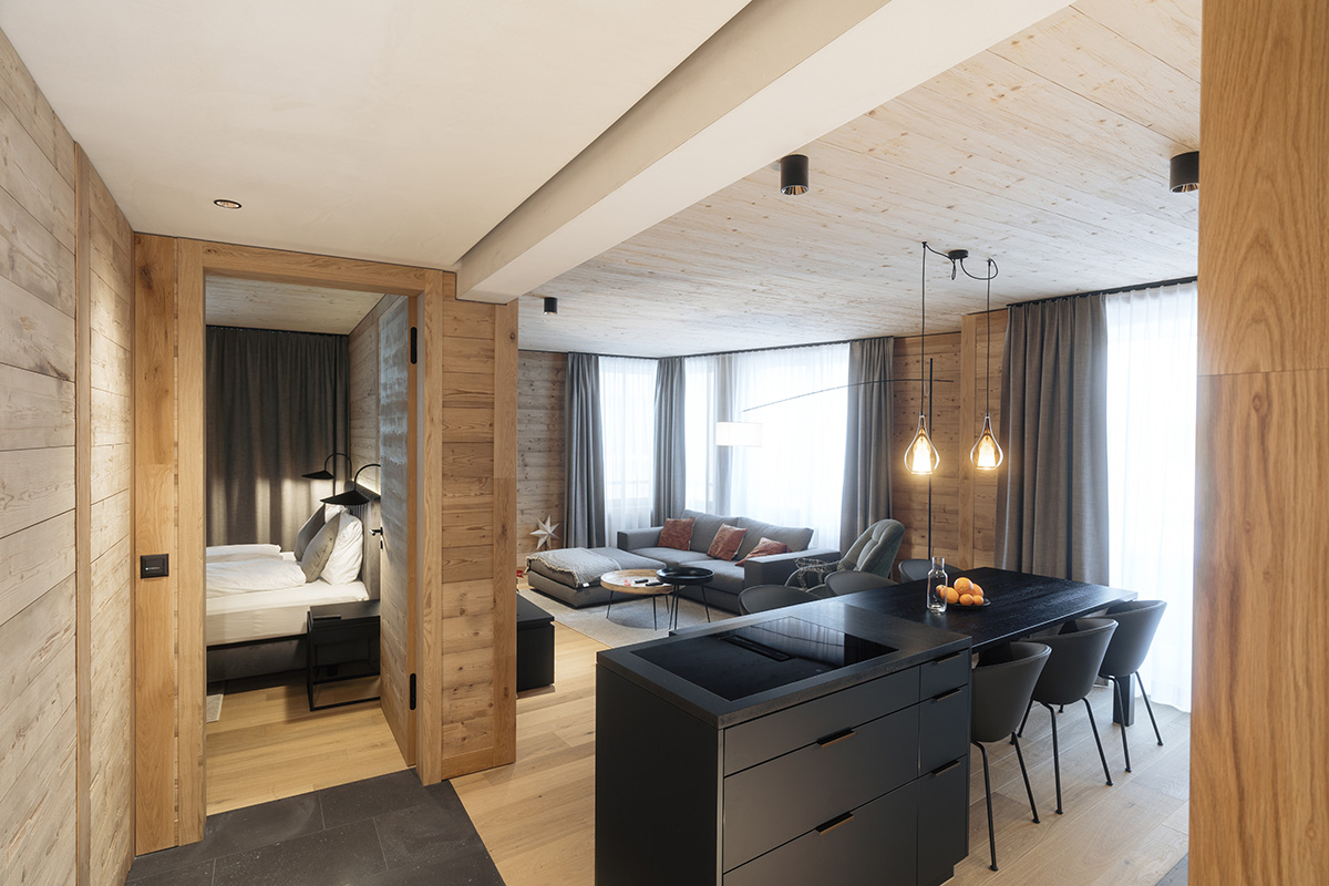 Modern vacation apartment in Andermatt in Switzerland with two bedrooms, windows, gray sofa, dark furniture and natural light.