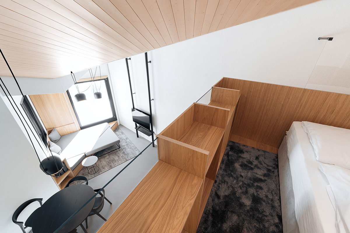 A bright vacation apartment in Switzerland with two sleeping areas, black furniture and two windows. View from the upper area.