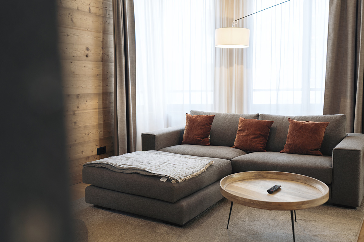 A gray comfortable couch in a vacation apartments in Switzerland with stylish design, large window and a round coffee table.