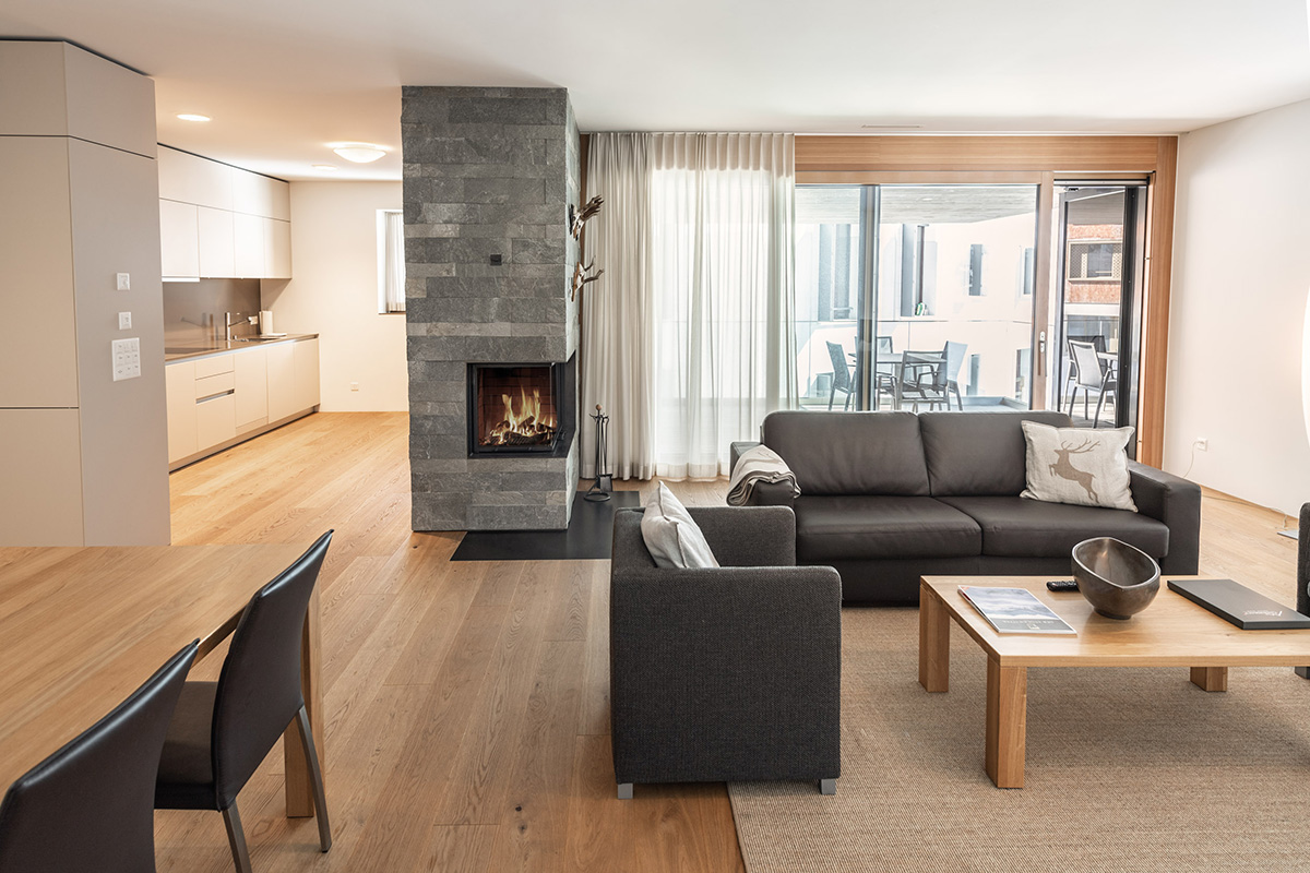 A large vacation apartment in Switzerland with gray furniture, a fireplace, sofa, coffee table, a white kitchen and terrace.