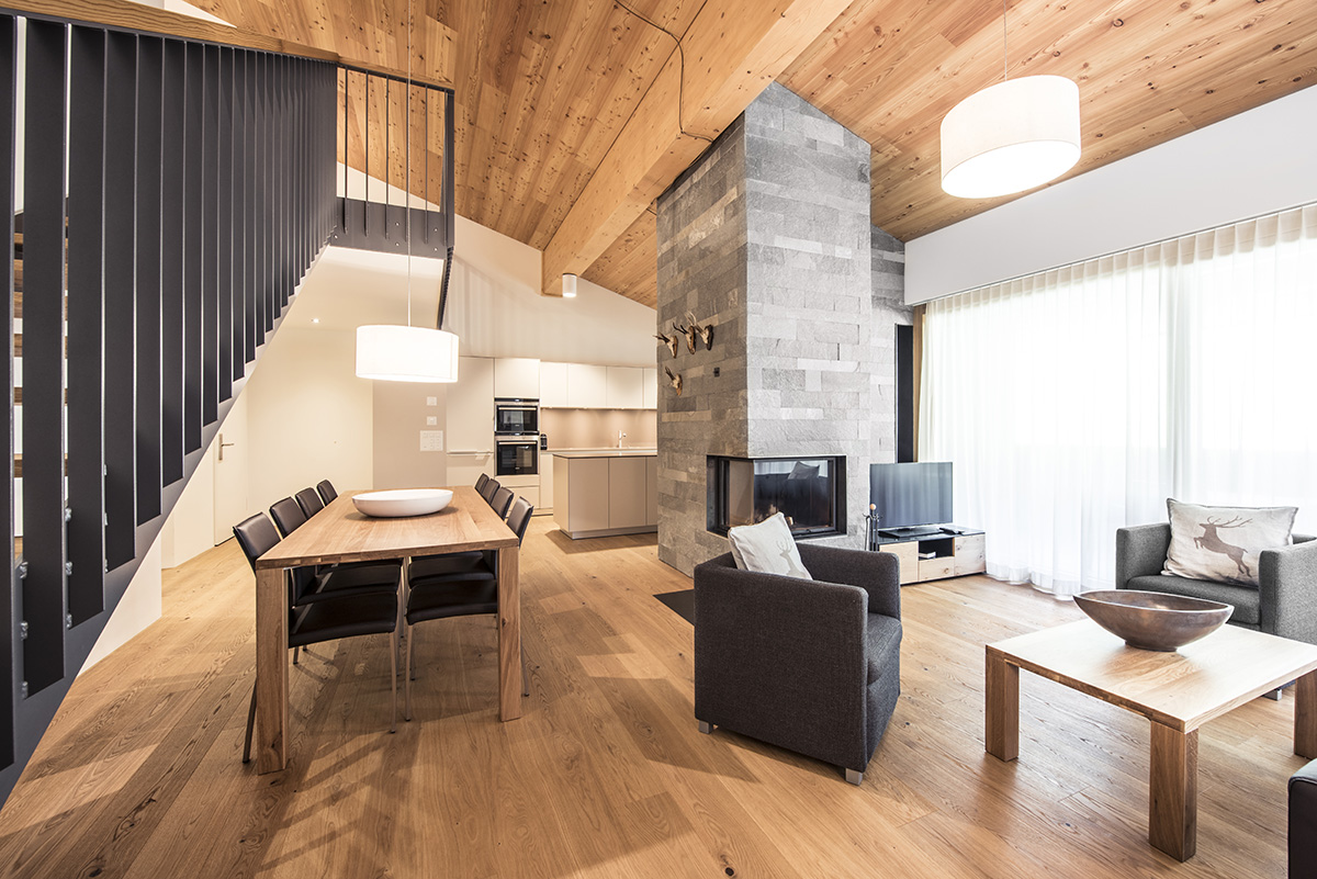 A large vacation apartment in Switzerland with two floors, a cozy sofa, wooden table, TV, kitchen and large windows.