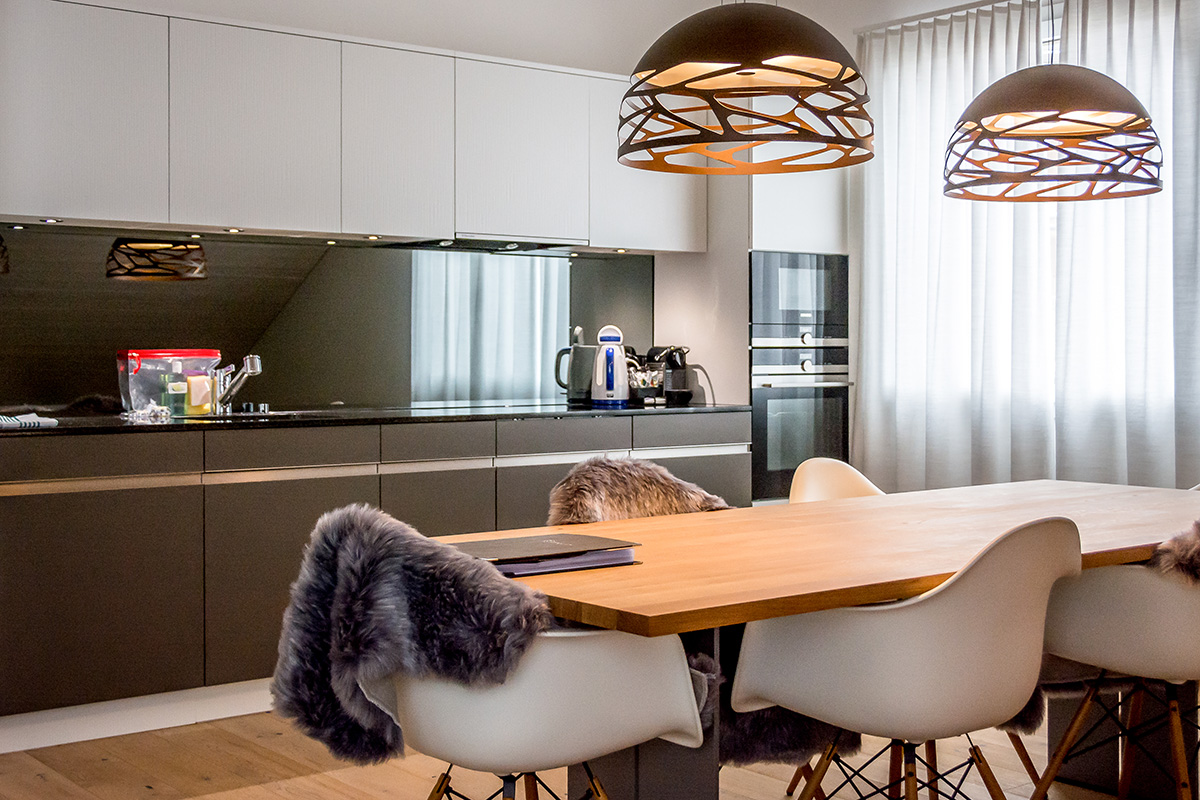 A modern large kitchen in gray tones in a vacation apartment in Switzerland, with a wooden table for six people and two lamps.