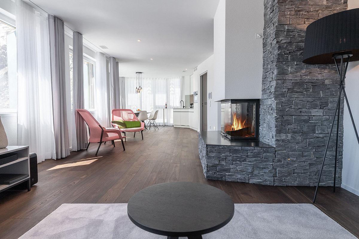 A vacation apartment in Switzerland with a cozy fireplace, round tables, dining area, pink armchairs and lots of light.