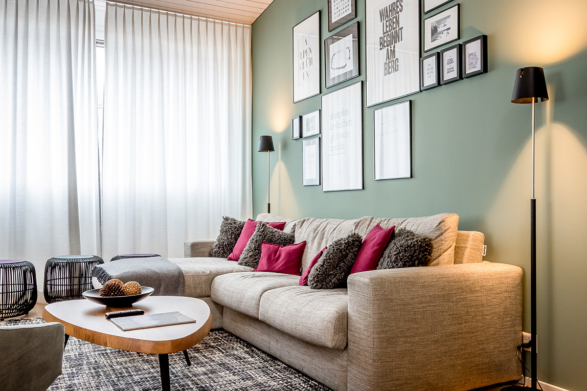 A vacation apartment in Switzerland with a cozy sofa, decorative cushions, murals and natural light through large windows.