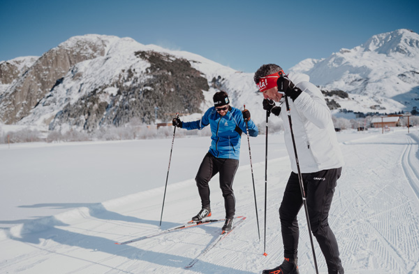 Two people are cross-country skiing in the snow, surrounded by mountains, on a winter holiday in a ski resort in Switzerland.