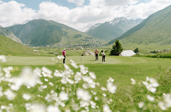 Three people playing golf amidst green meadows and mountains, on their summer vacation in Switzerland with breathtaking nature.