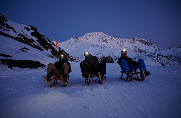 Three people, spending their winter holiday in Switzerland, are skiing at night with sledges in the ski resort.