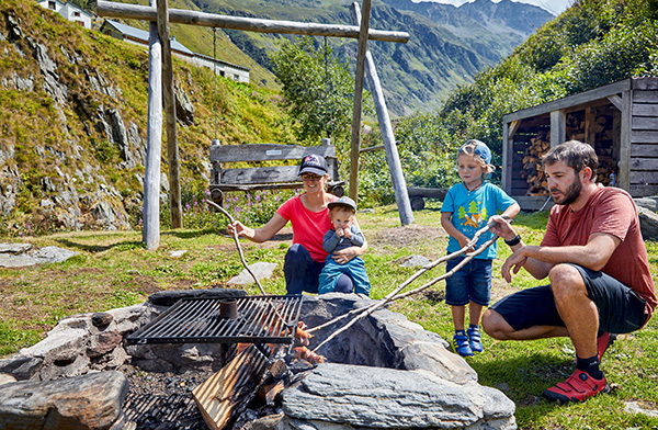 A couple with two children on a relaxing family vacation in Switherland is having an outdoor barbecue in the mountains.