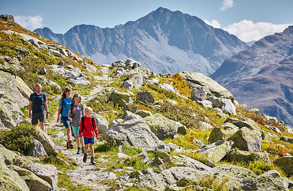 Children and adults hiking on a mountain path, surrounded by impressive nature, on their summer vacation in Switzerland.