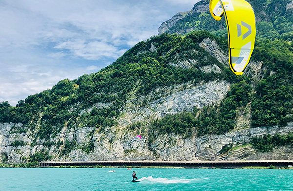 A kitesurfer on a lake with an impressive mountain backdrop - an exciting activity on a summer vacation in Switzerland.