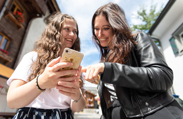 Two women laugh and look at their cell phones during a family vacation in Switzerland.