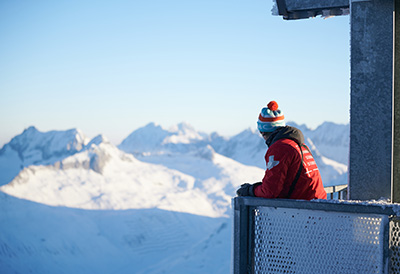 A person in warm clothing stands on a balcony and looks out over snow-covered mountains in Switzerland.