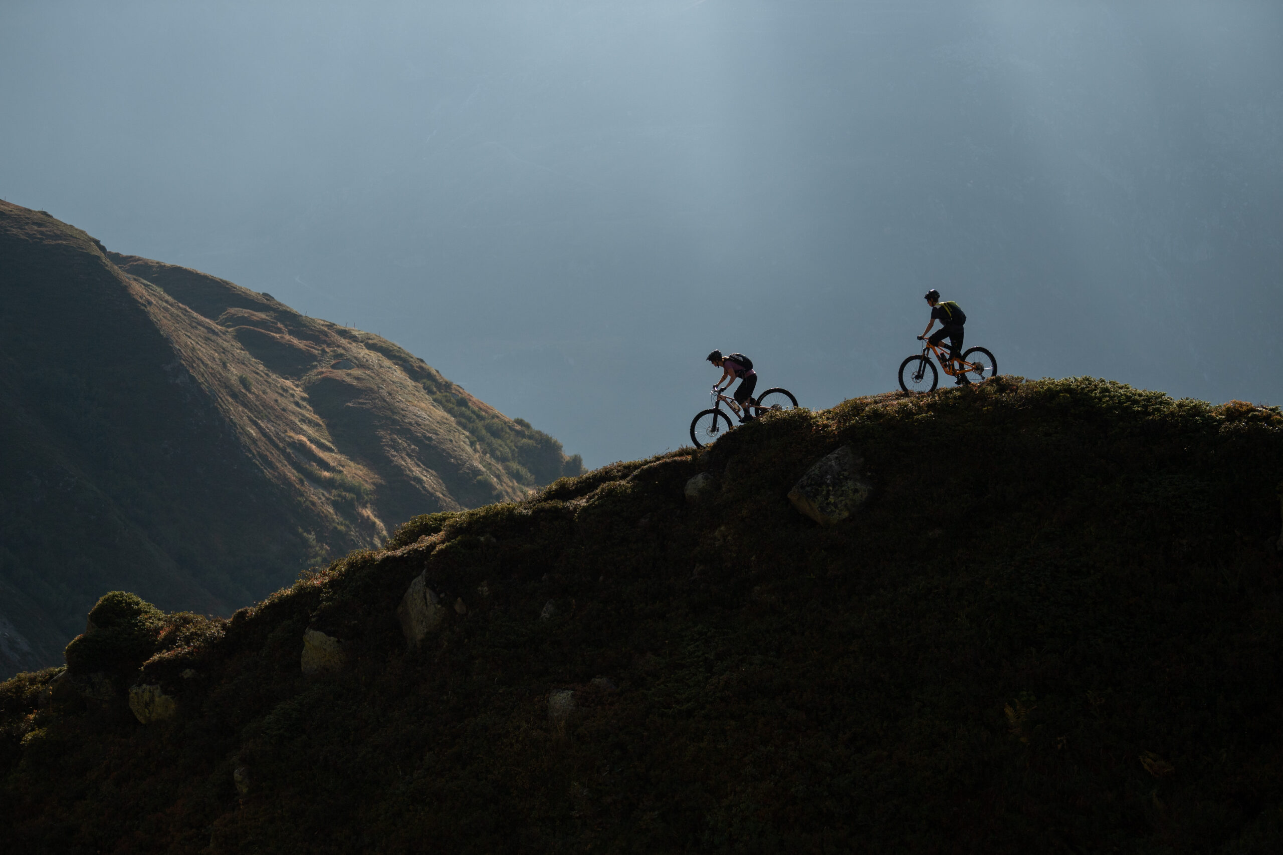 Mountain bikers riding a ridge trail above Andermatt at sunset
