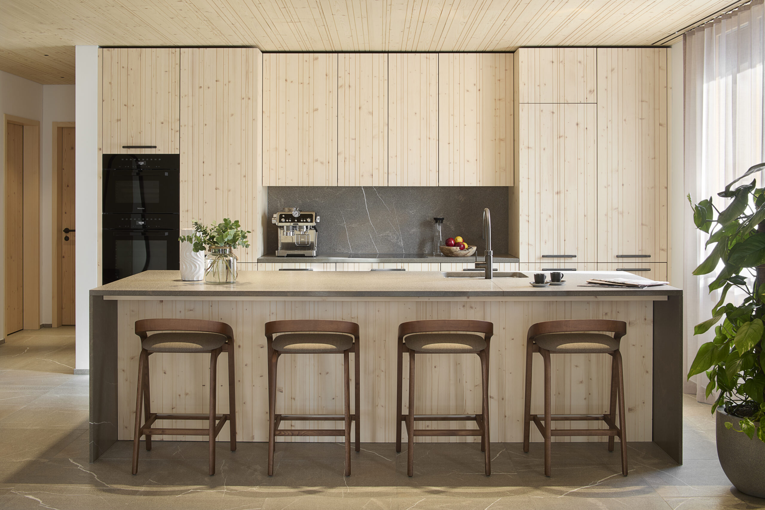 Open-plan kitchen with wood paneling and island seating at Andermatt Alpine Apartments